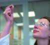 Frau mit längeren braunen Haaren und Schutzbrille, die eine kleine weiße Nanoperle in der Hand hält. Sophia Pews betrachtet eine offenzellige Nanoperle, für die sie ein neues Verfahren zur Verschweißung mitentwickelt hat.
