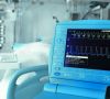 Ein Monitor in einem Krankenzimmer mit Anzeige Herzfrequenz usw. umrahmt von einem blauen Plastikrahmen mit Bedienungselementen.