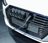 Motorgrill eines weißen Audis in dem ein Ladekabelstecker hängt. Um in Elektrofahrzeugen Gewicht zu sparen, werden Kunststoffe eingesetzt.