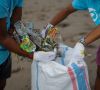 zwei Menschen stecken am Strand gesammelten Müll in einen Sack