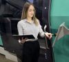 junge Frau mit langen braunen Haaren steht vor einer Maschine und bedient die Steuerung